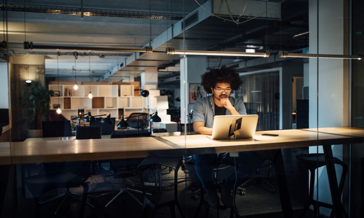 Mann sitzt noch spät abends im Büro und arbeitet am Laptop.