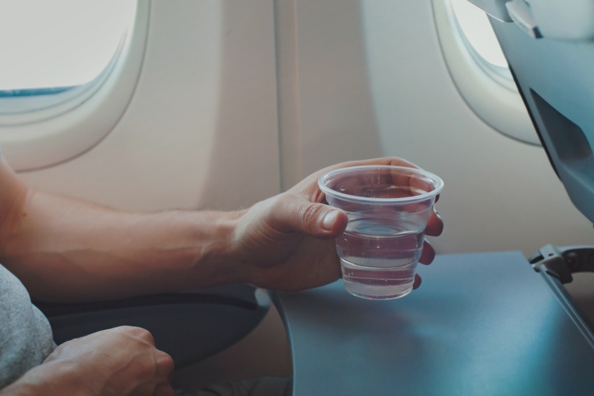 Mann hält einen Becher Wasser im Flugzeug
