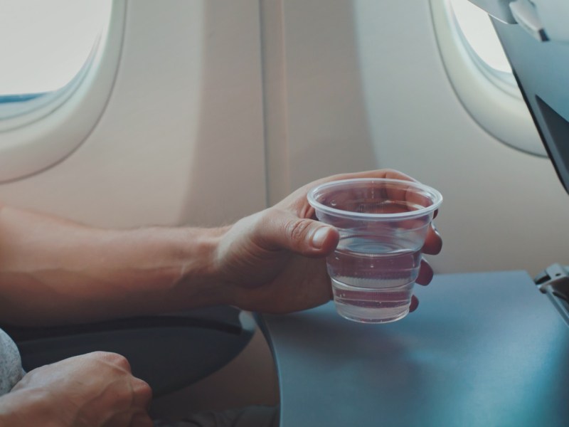 Mann hält einen Becher Wasser im Flugzeug