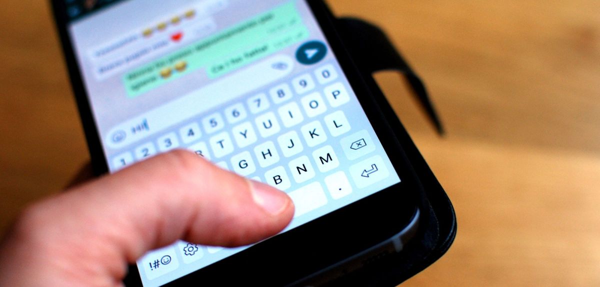 Person hält Handy mit geöffnetem WhatsApp-Textfenster in der Hand.