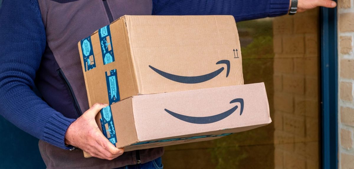 Mann hält Amazon-Pakete im Arm und klingelt an Tür.