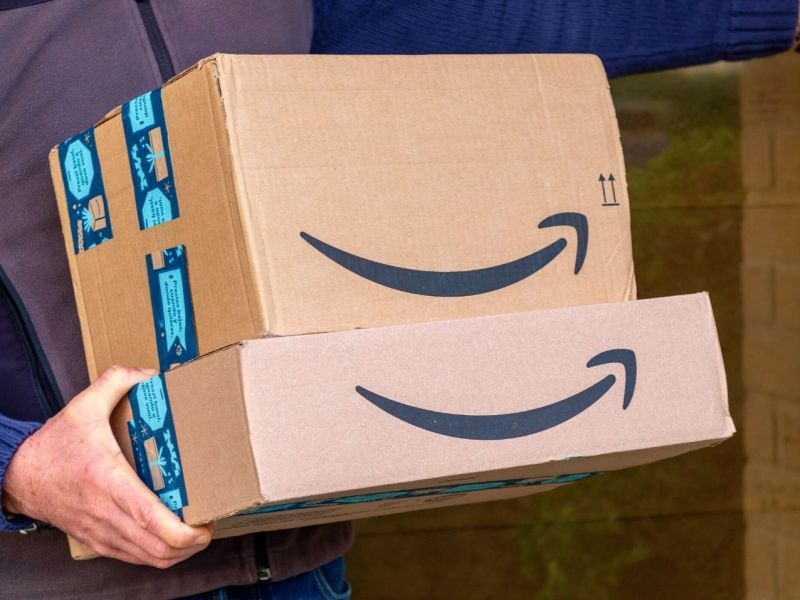 Mann hält Amazon-Pakete im Arm und klingelt an Tür.