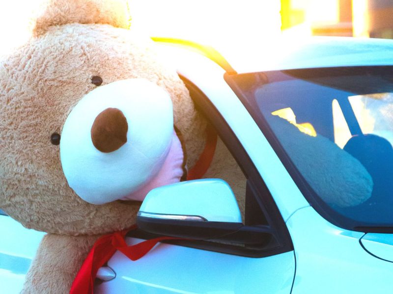 Riesiger Teddybär sitzt in einem Auto und hängt halb aus dem Fenster.