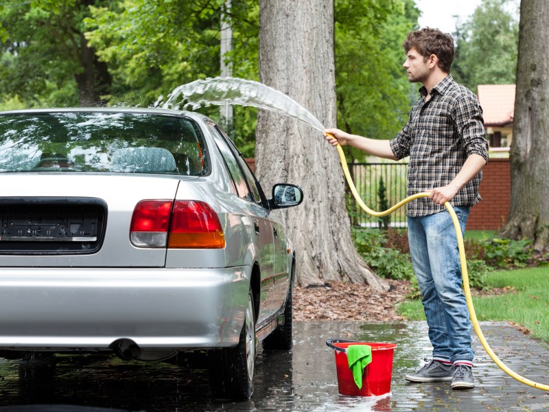 Auto wird im Garten von Mann gewaschen