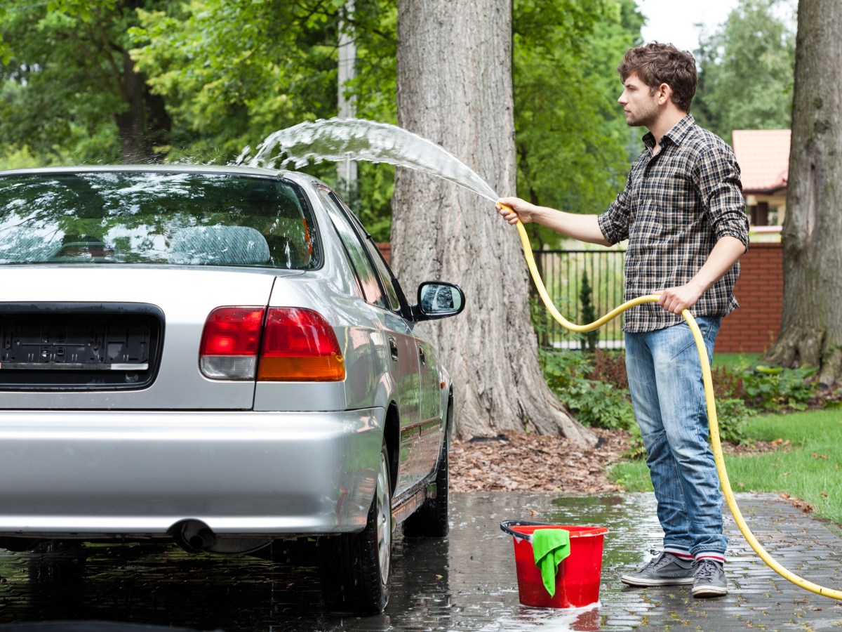 Auto wird im Garten von Mann gewaschen