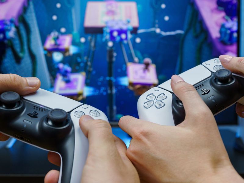 Zwei Personen spielen PS5 mit DualSense-Controllern.