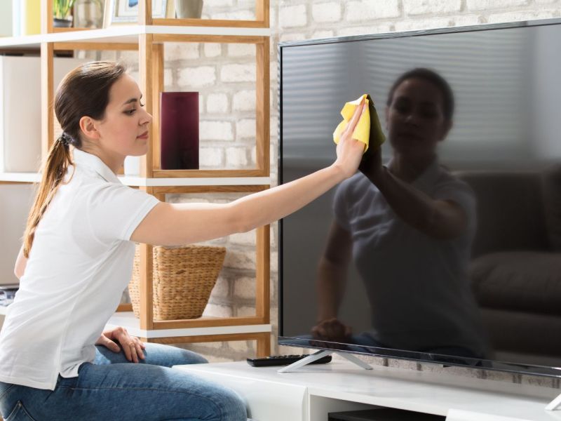 Frau reinigt Fernseher im Wohnzimmer.