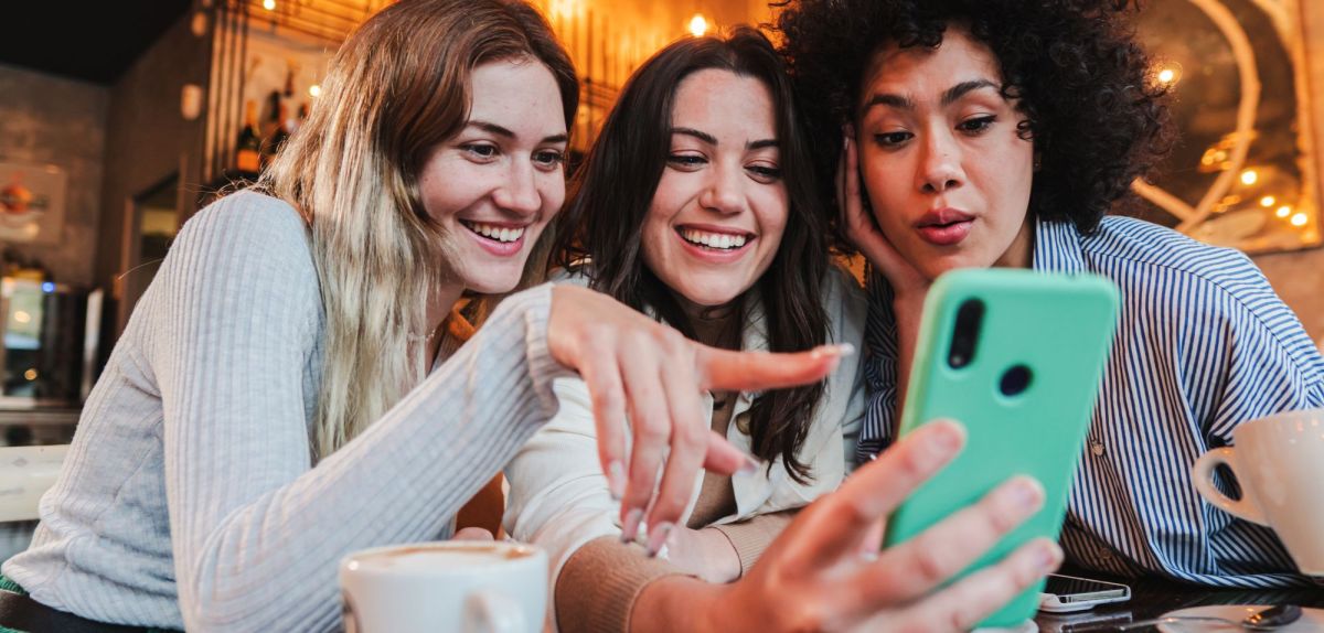 Drei Frauen schauen auf ein Handy und freuen sich