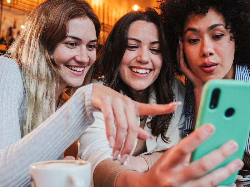 Drei Frauen schauen auf ein Handy und freuen sich