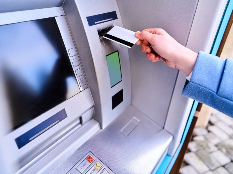 Mann hält EC-Karte vor einen Geldautomaten
