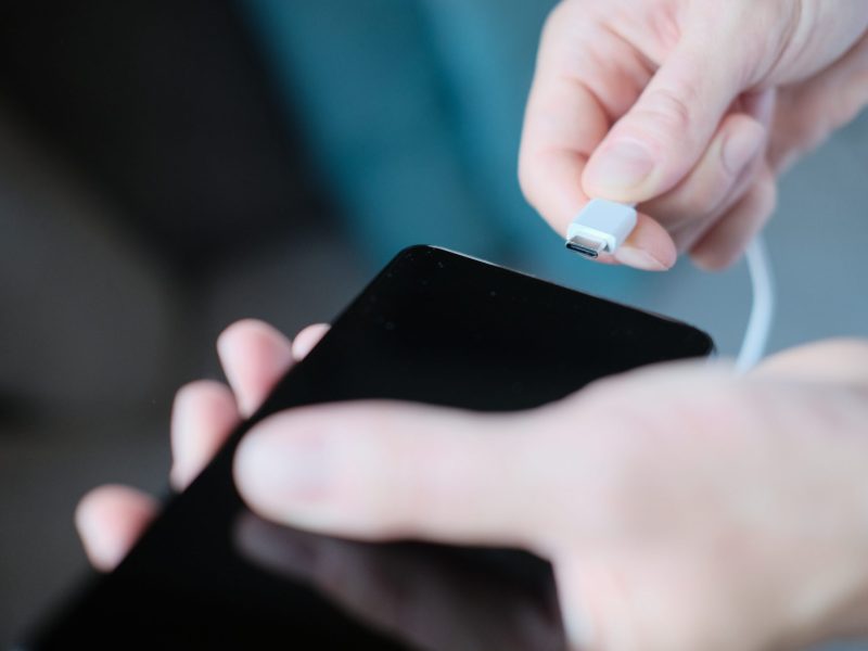 Person schließt Ladekabel an ein Smartphone an.