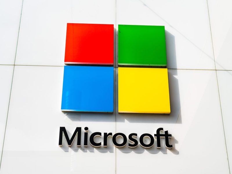 Das Logo von Microsoft hängt an einer weißen Hauswand.