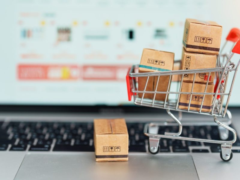 Symbolbild für Online-Shopping: Mit Paketen gefüllter Mini-Einkaufswagen steht auf Laptoptastatur.