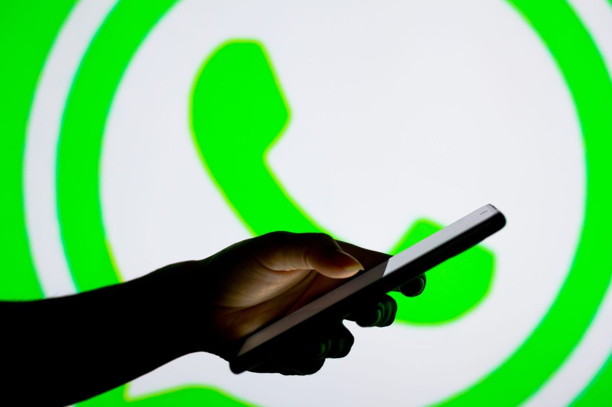 Eine Person hält ein Handy in der Hand, während im Hintergrund das WhatsApp Logo erscheint.