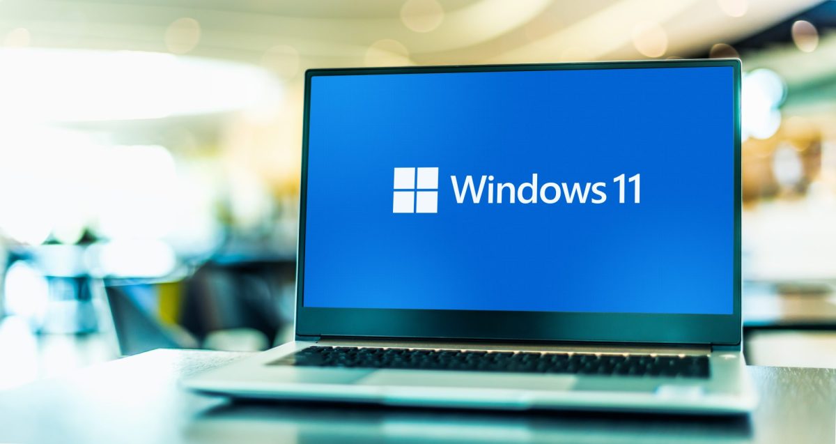 Das Windows 11 Logo auf dem Bildschirm eines Laptops im Büro stehend.