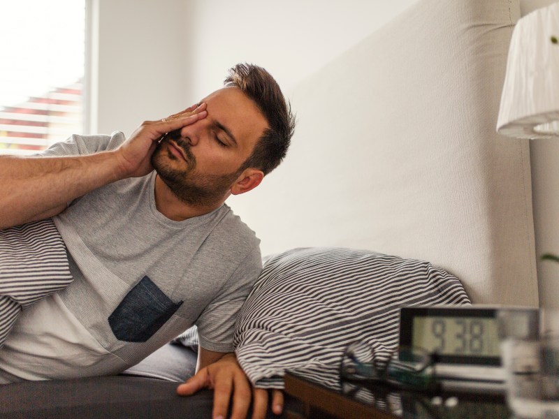 Mann liegt verschlafen im Bett