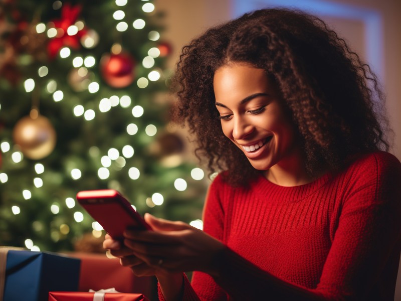 Frau mit Smartphone vor einem Weihnachtsbaum