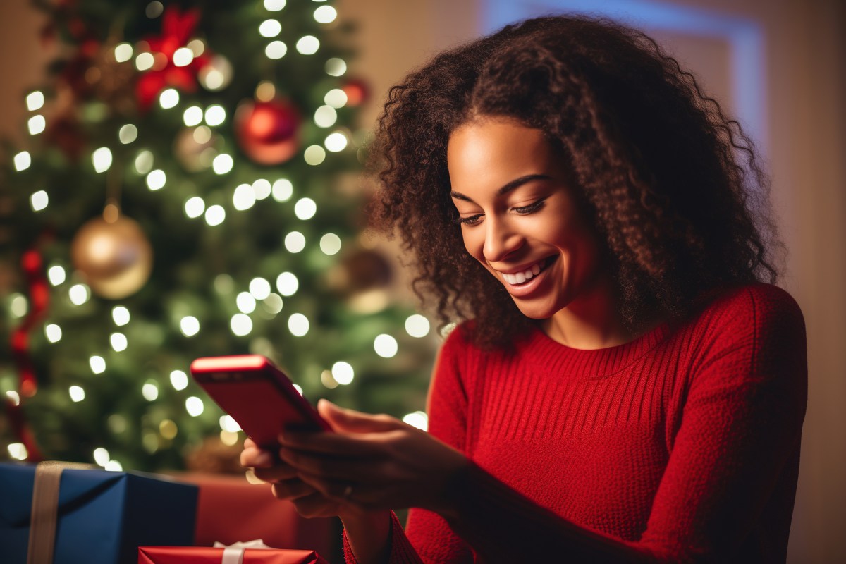 Frau mit Smartphone vor einem Weihnachtsbaum