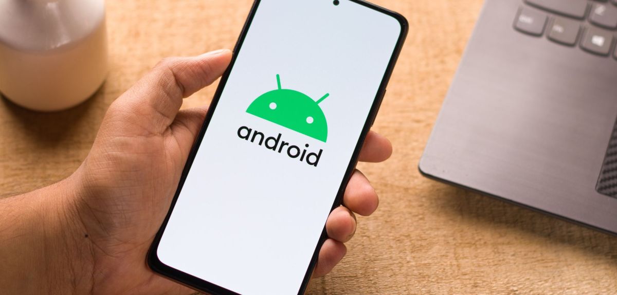 Person hält Smartphone mit Android-Logo in der Hand.