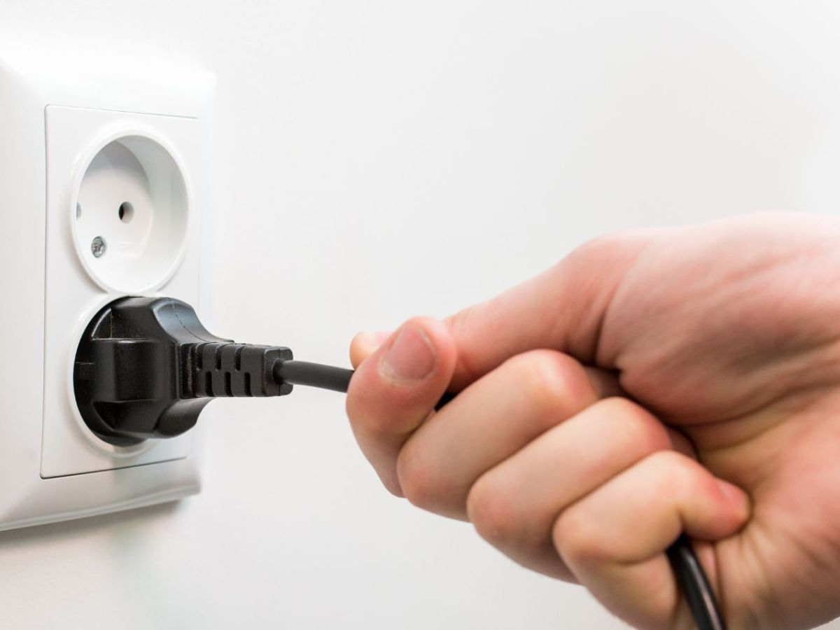 Hand zieht Netzstecker aus der Steckdose.