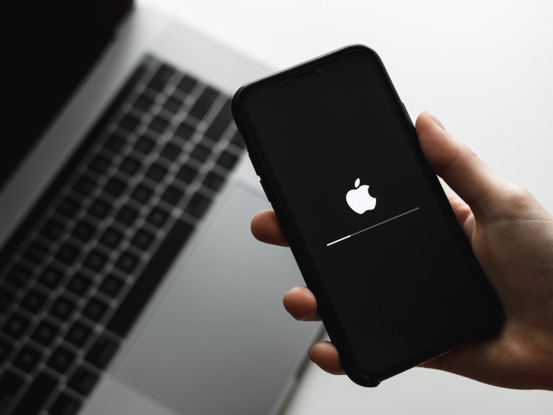 Ansicht von iPhone-Update auf einem iPhone, gehalten von einer Hand über einem Laptop.