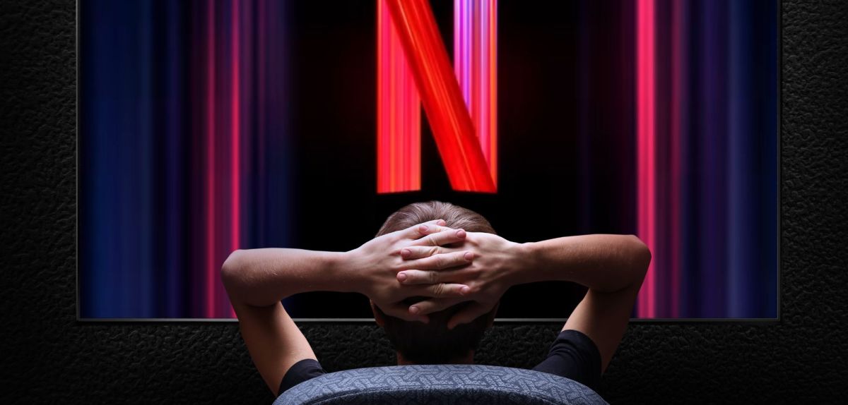 Person sitzt vor einem gigantischen Bildschirm mit dem Netflix-Logo.