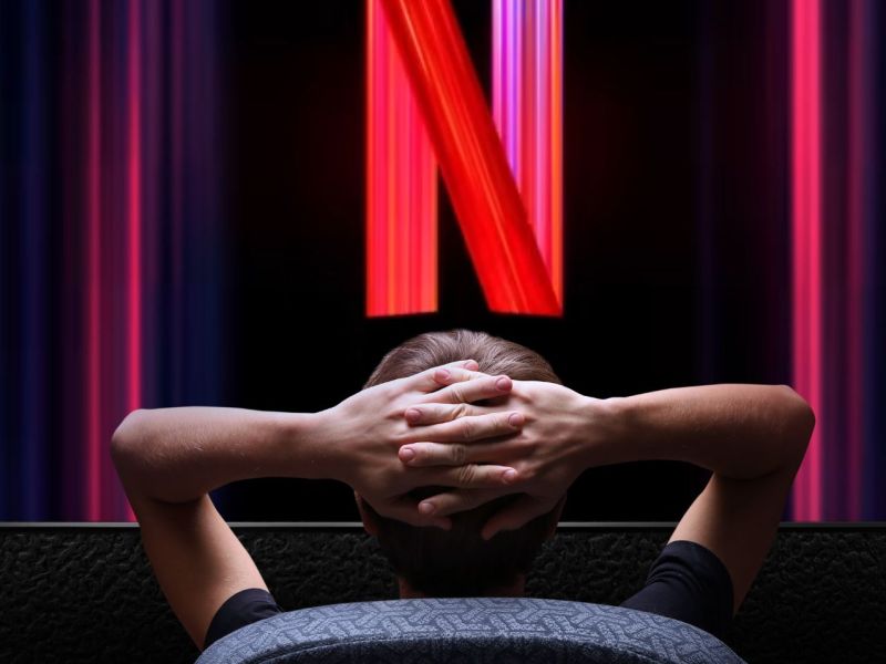 Person sitzt vor einem gigantischen Bildschirm mit dem Netflix-Logo.
