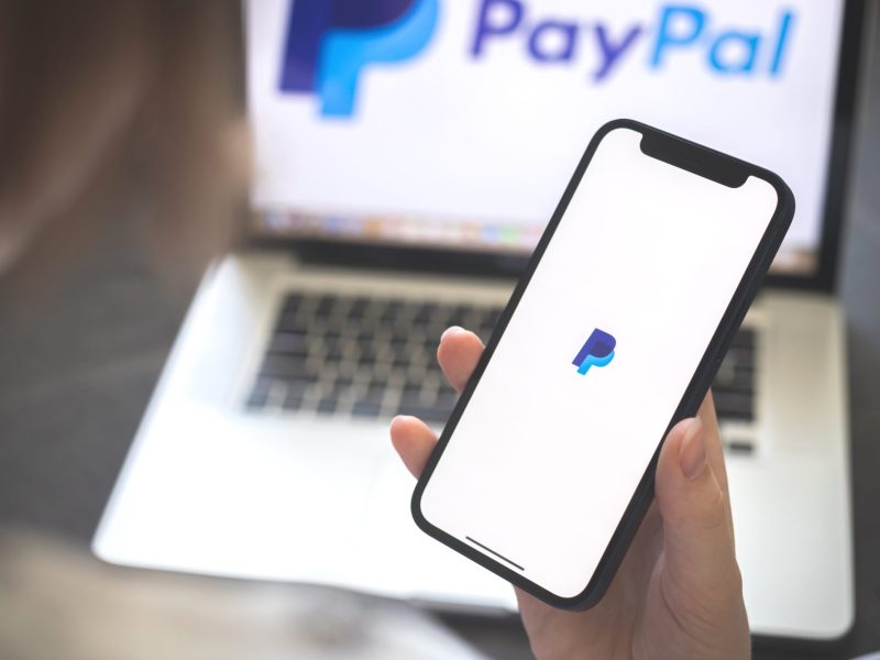 Eine Person nutzt PayPal auf Laptop und Smartphone.