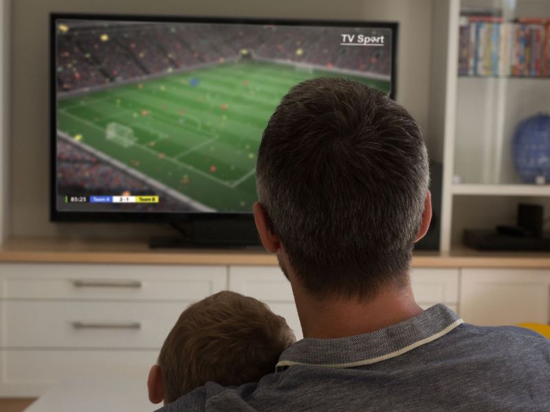 Vater und Sohn schauen Fernsehen über Satellit oder Kabel.