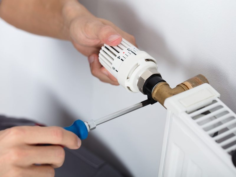 Hand bedient ein Thermostat an der Heizung.