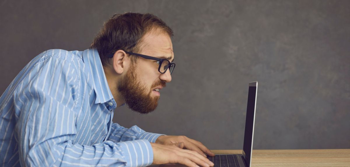 Mann schaut besorgt und erschrocken auf einen Laptop-Bildschirm.