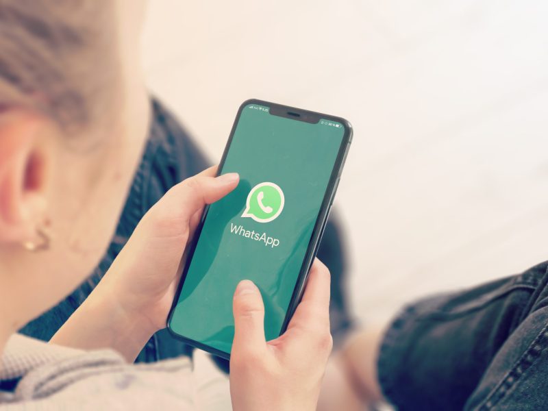 Person tippt auf Smartphone-Bildschirm, auf dem WhatsApp geöffnet ist.