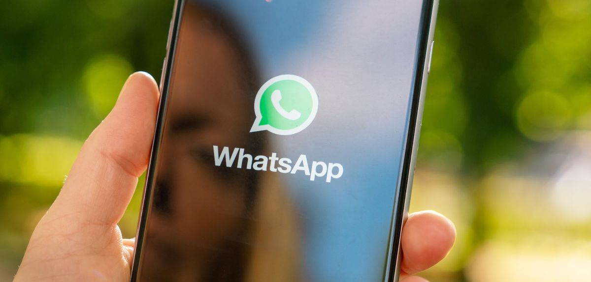 WhatsApp-Logo auf einem Handy, das eine Person in der Hand hält.