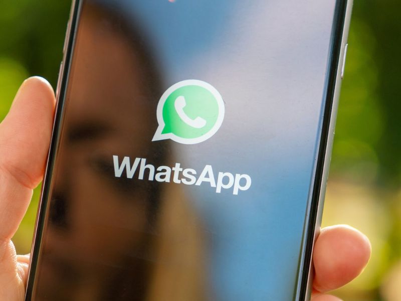 WhatsApp-Logo auf einem Handy, das eine Person in der Hand hält.