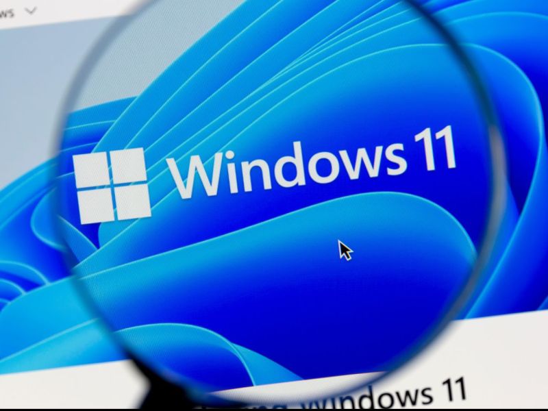 Windows 11-Logo auf einem Screen unter einer Lupe.
