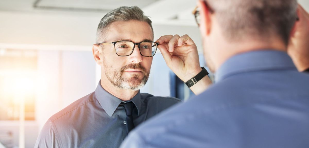 Mann schaut in den Spiegel mit Brille