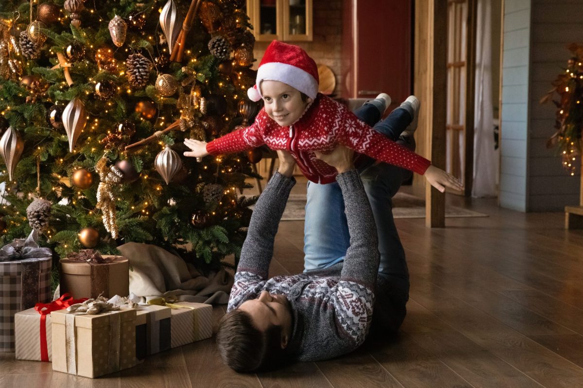 Mann spielt vor einem Weihnachtsbaum mit einem Kind Flugzeug