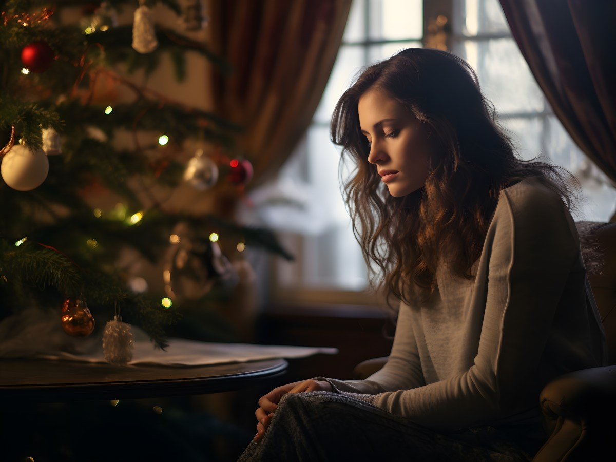 Frau sitzt mit enttäuschtem Gesicht vor einem Weihnachtsbaum.