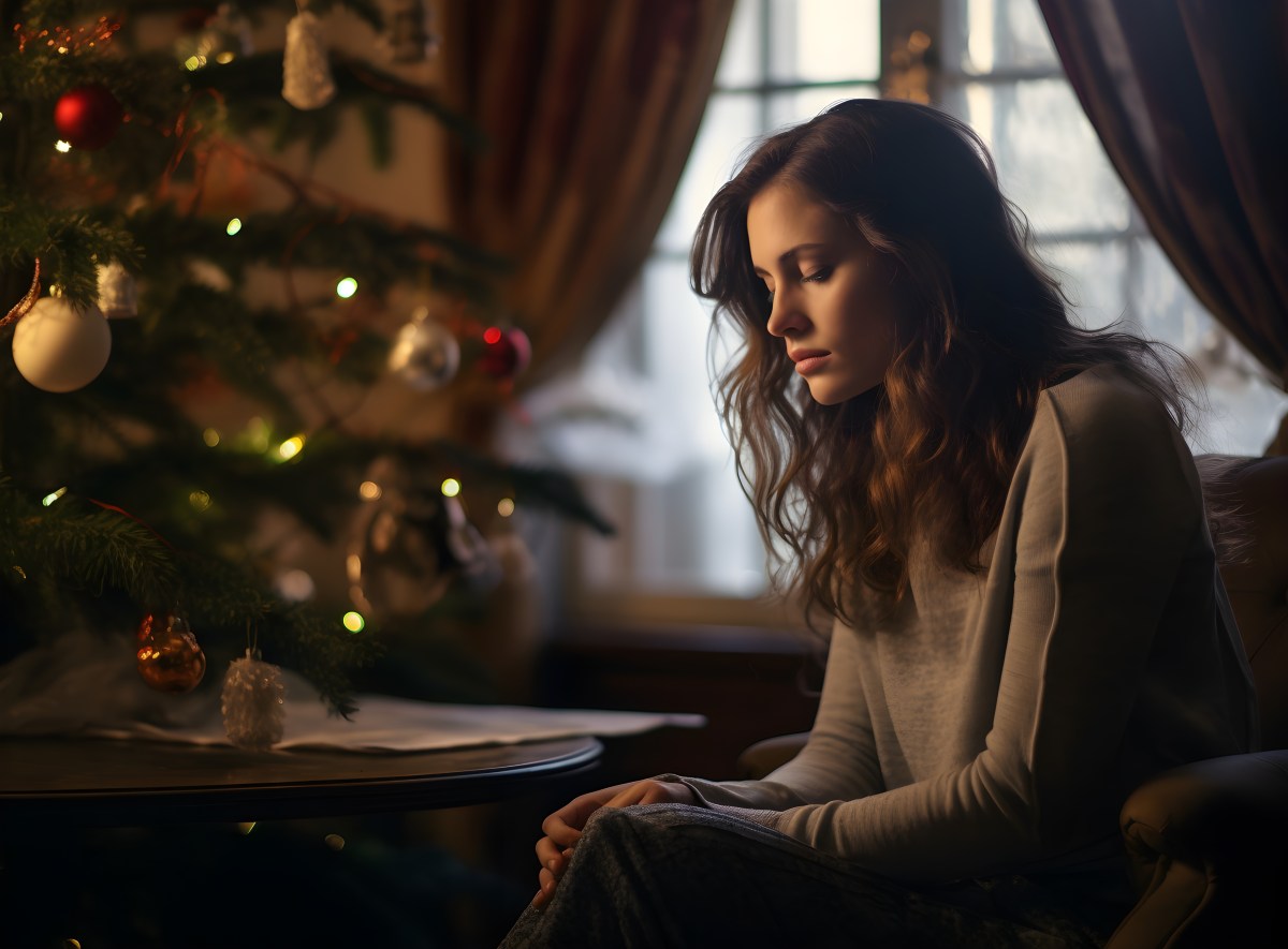 Frau sitzt mit enttäuschtem Gesicht vor einem Weihnachtsbaum.