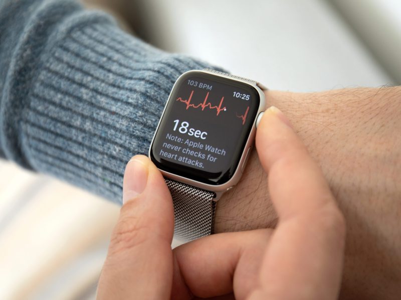 Apple Watch zeigt Herzfrequenz an, befestigt an einem Handgelenk, während zwei Finger die Uhr halten.