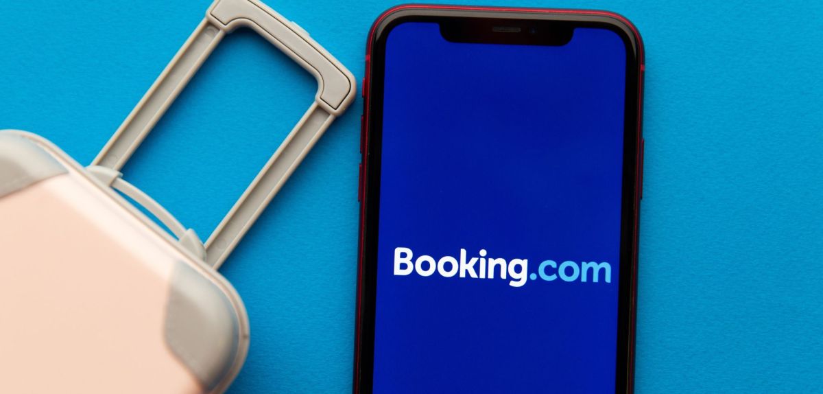 Booking.com-Schriftzug auf einem Handy, daneben ein Koffer.