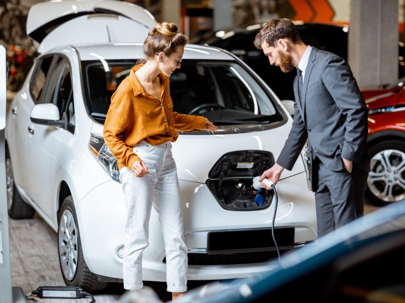 Ein Händler führt seiner Kundin ein neues Elektroauto vor.