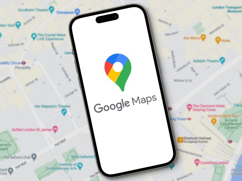 Das Logo von Google Maps erscheint auf einem Smartphone während im Hintergrund eine große Karte zu sehen ist.