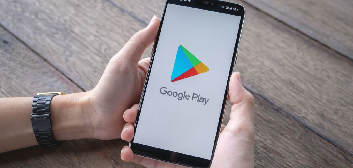 Person hält Handy mit dem Google Play Store auf dem Bildschirm in der Hand.