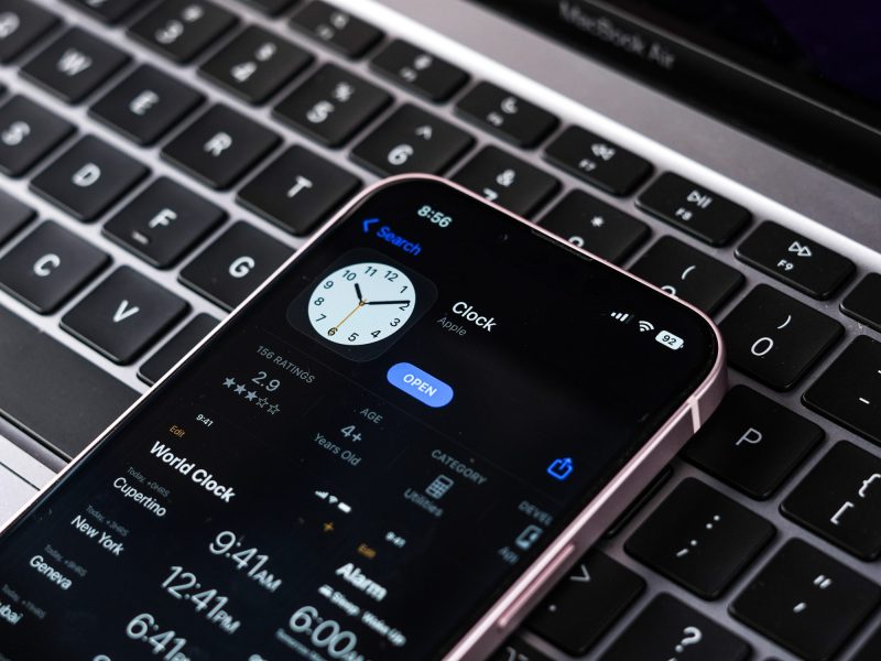 iPhone liegt auf Laptoptastatur und zeigt Uhr an.