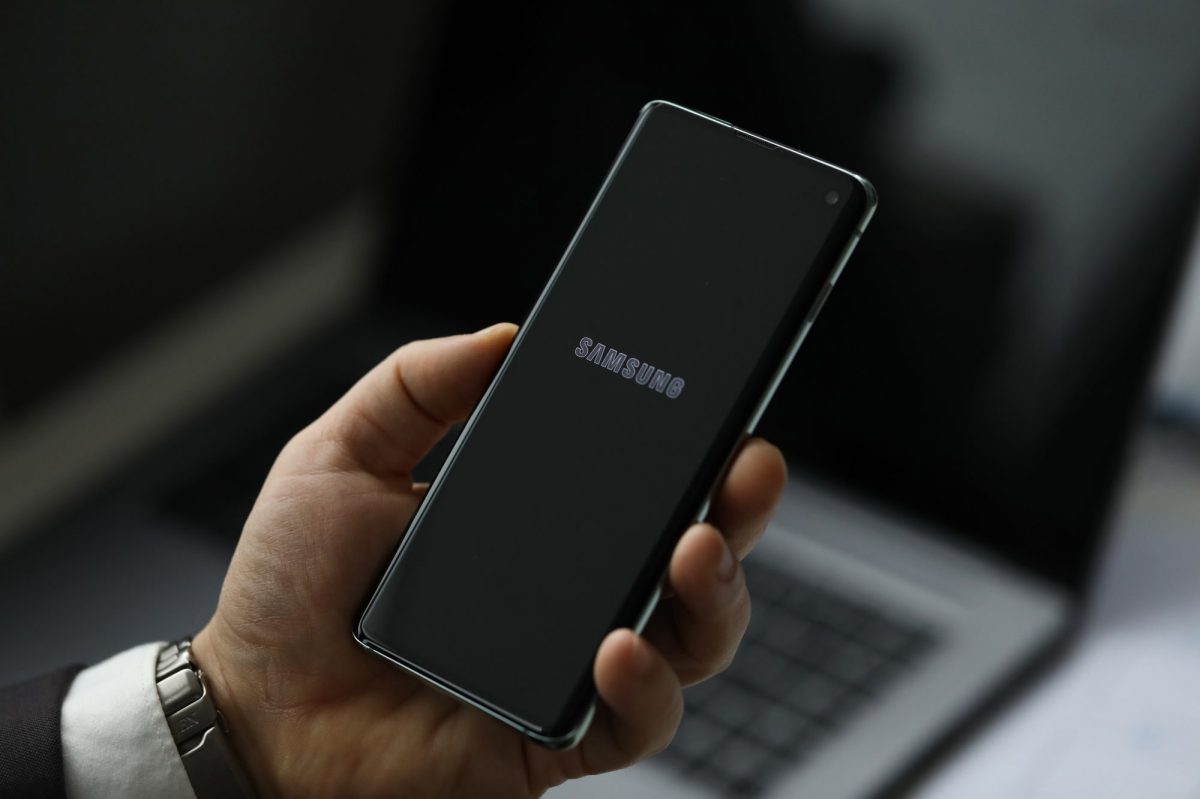 Ein Samsung-Handy wird von einer Hand vor einem Laptop gehalten.