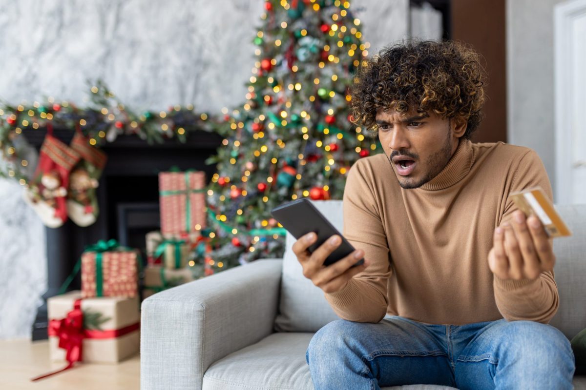 Ein Mann starrt an Weihnachten erbost auf sein Handy und seine Kreditkarte.