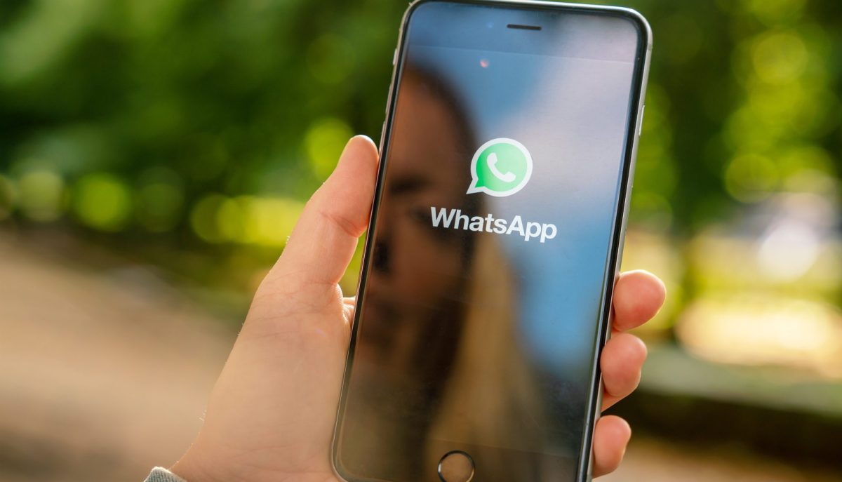 Eine blonde Frau spiegelt sich auf ihrem Smartphone während sie WhatsApp öffnet.