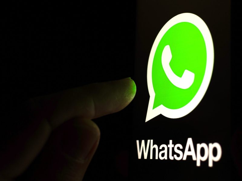 Ein Finger berührt ein riesiges WhatsApp-Logo im Dunklen.