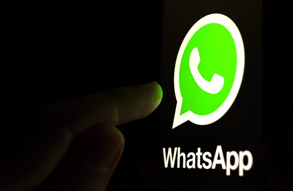 Ein Finger berührt ein riesiges WhatsApp-Logo im Dunklen.